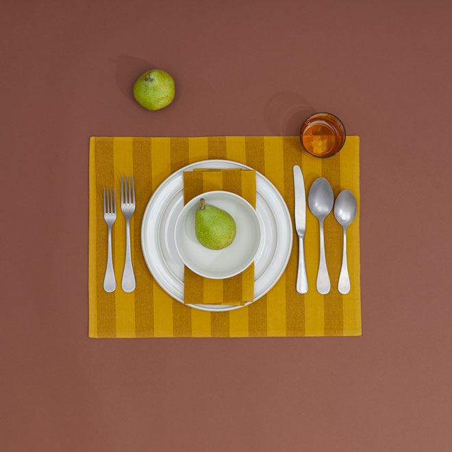 place setting including white plates and bowl, flatware, yellow striped napkin and placemat on brown background