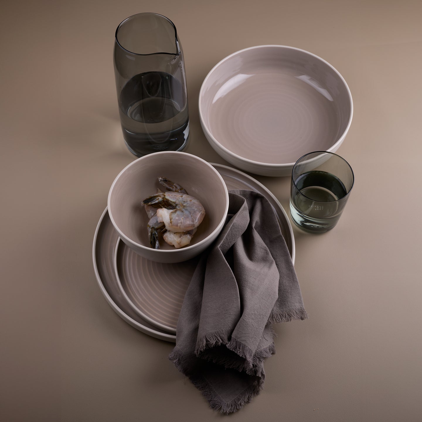 Essential dinnerware, glassware, pitcher, and napkins in Grey tones.