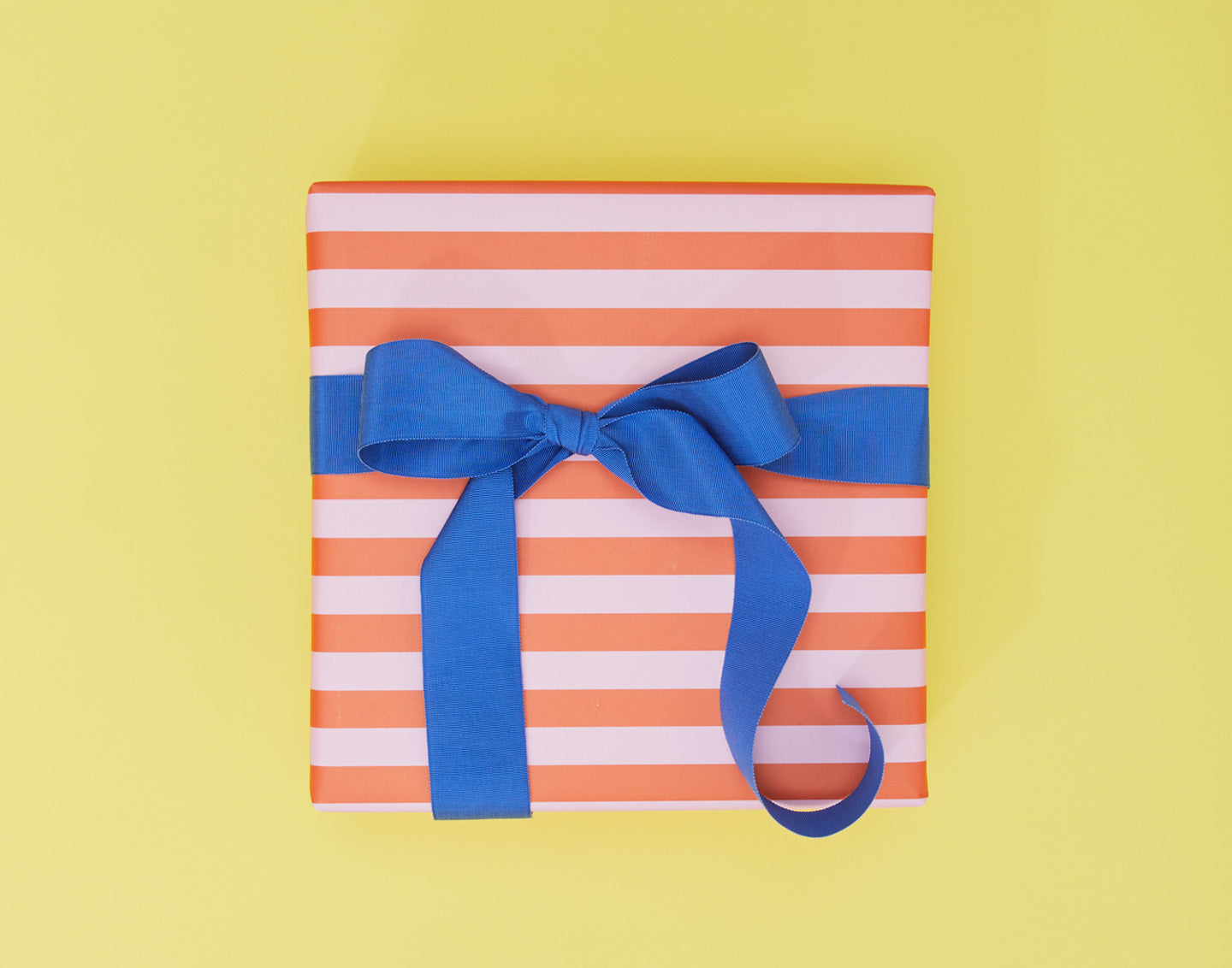 Box wrapped with orange and pink striped wrapping paper and a blue ribbon