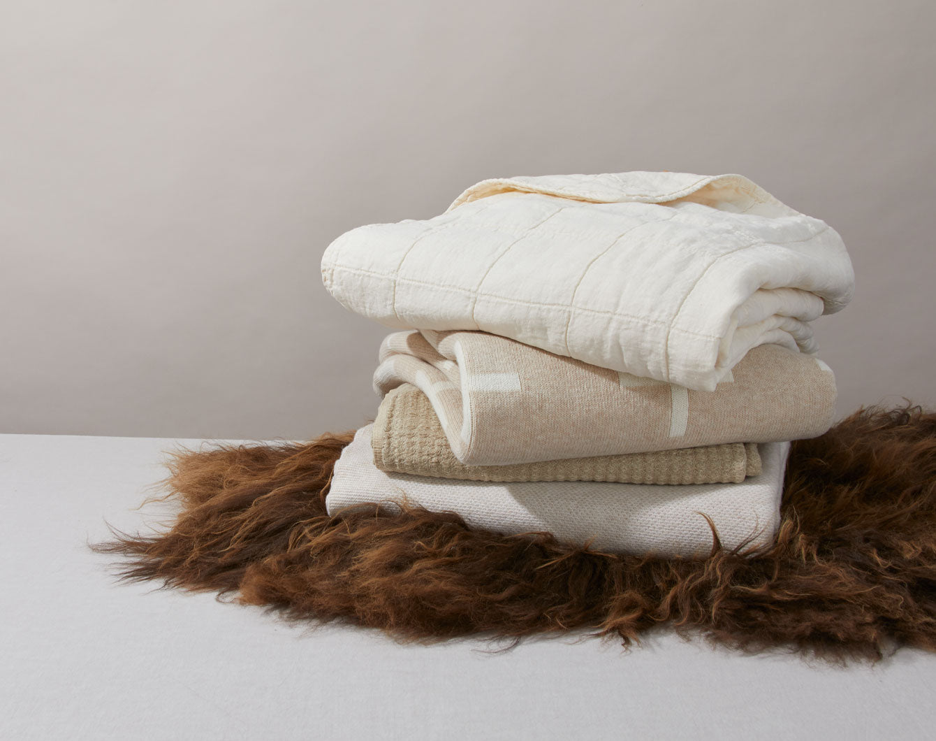 stack of ivory and flax colored throws on a brown sheepskin rug