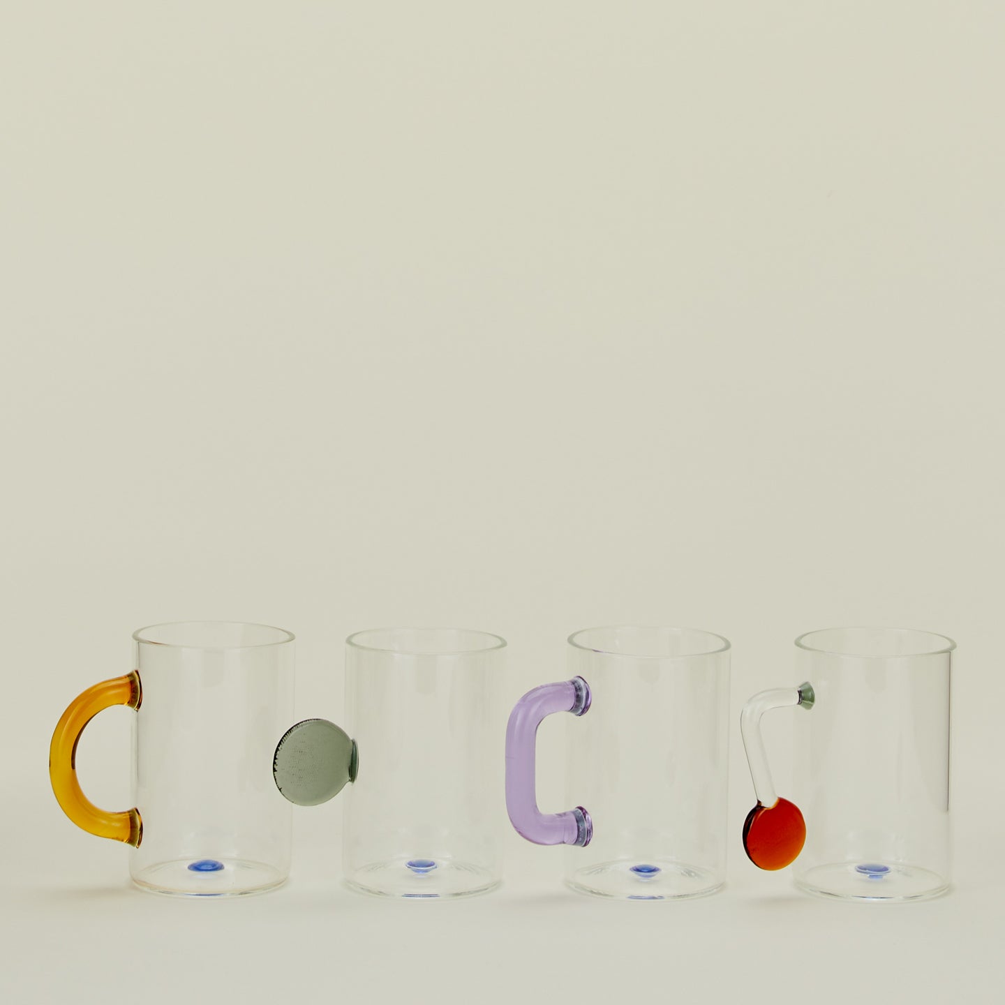 Set of four clear glass tea cups with assorted colored and shaped handles.