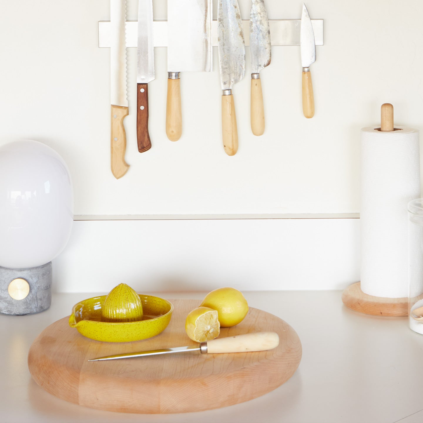 Kitchen counter with knives, paper towel holder, lamp, cutting board, lemons, and stoneware citrus juicer in Yellow.