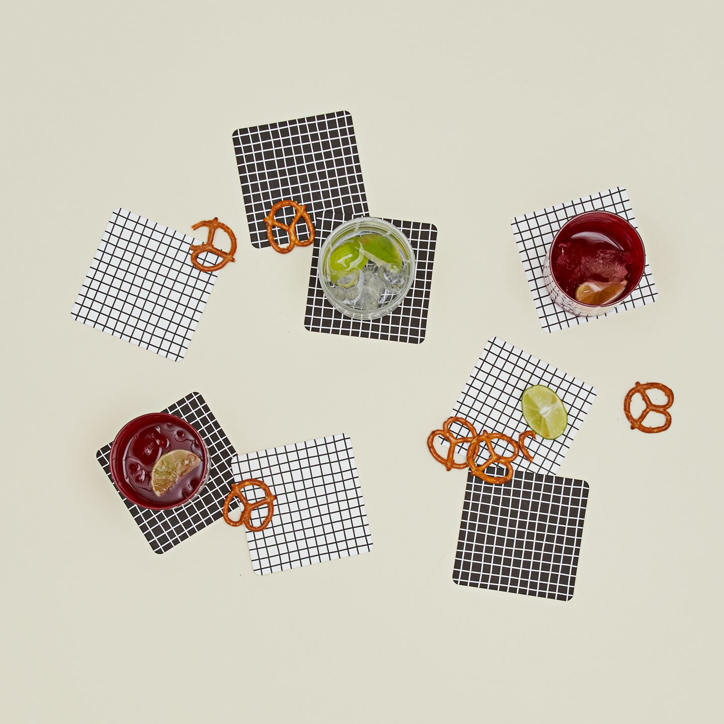 Set of eight reusable gridded paper coasters with glassware and snacks.