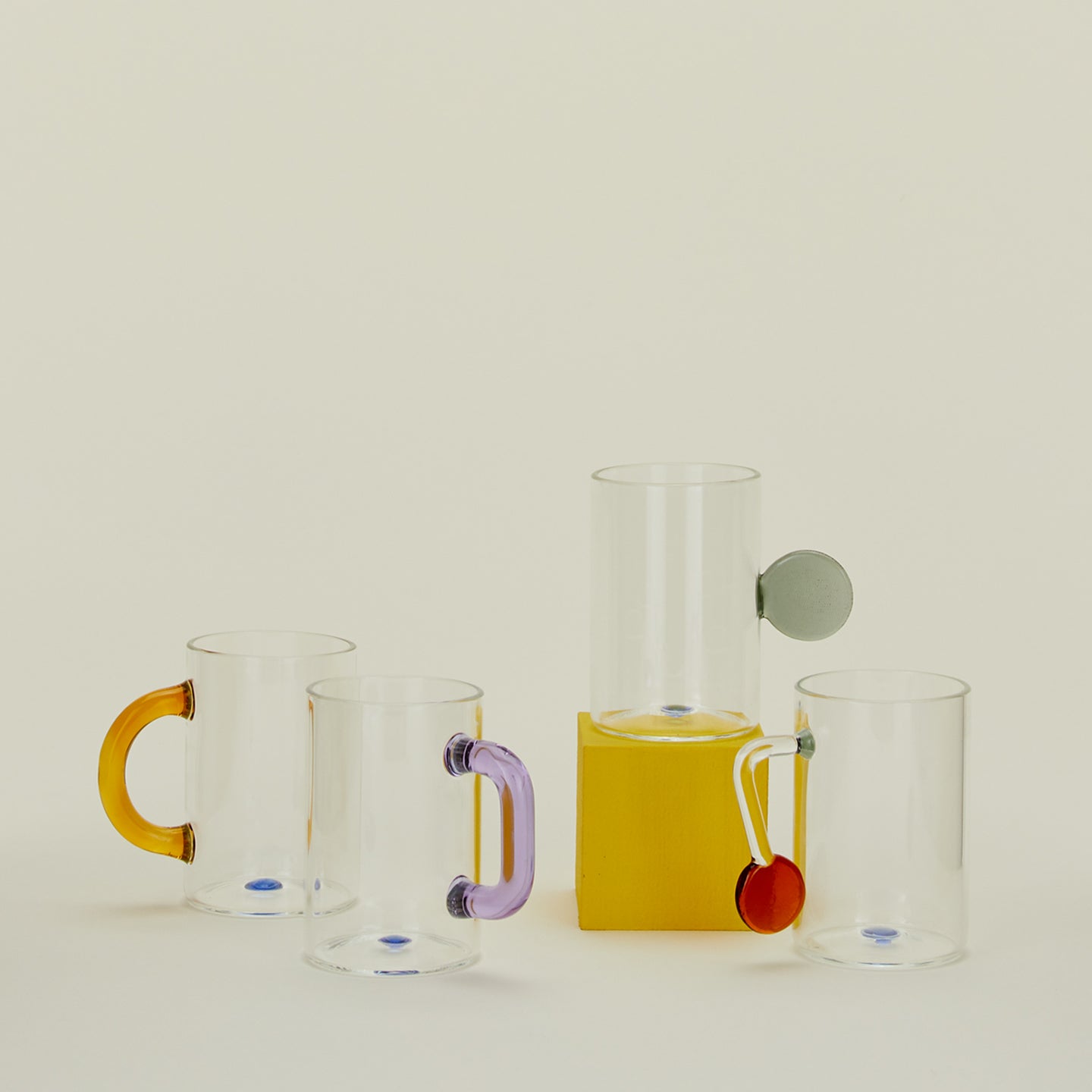 Set of four clear glass tea cups with assorted colored and shaped handles.