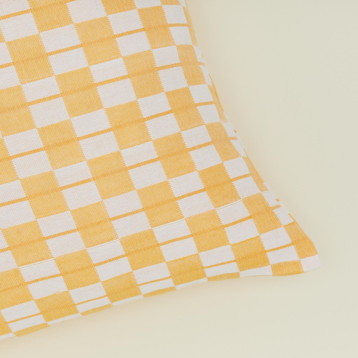 Corner detail of quilted checkered pillow in yellow and white.