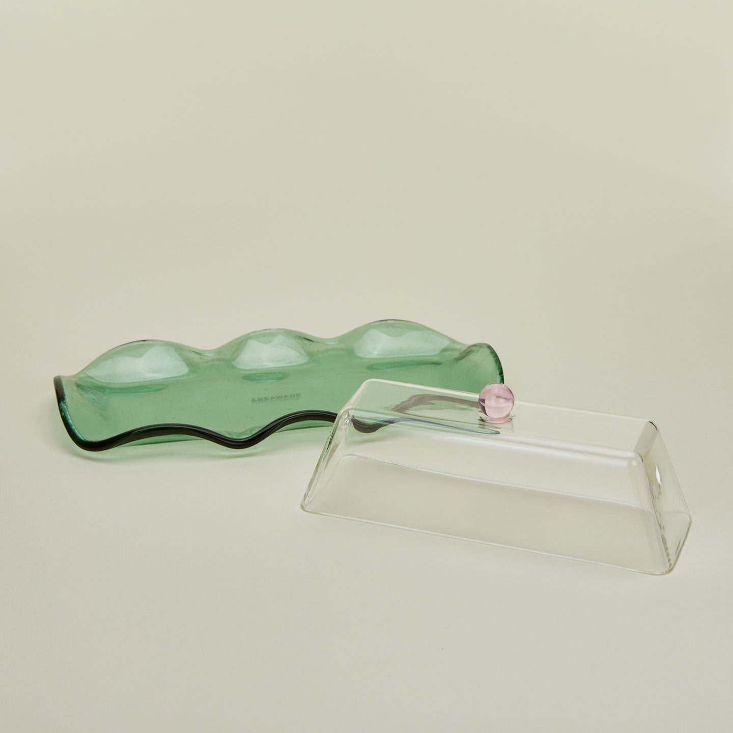 Close up of glass butter dish with a green tray and clear lid with a pink knob.