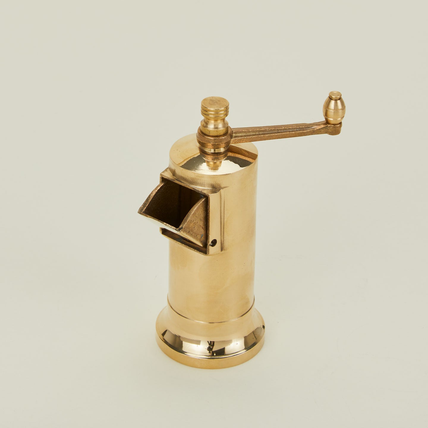 A close up of a brass spice grinder with handle.