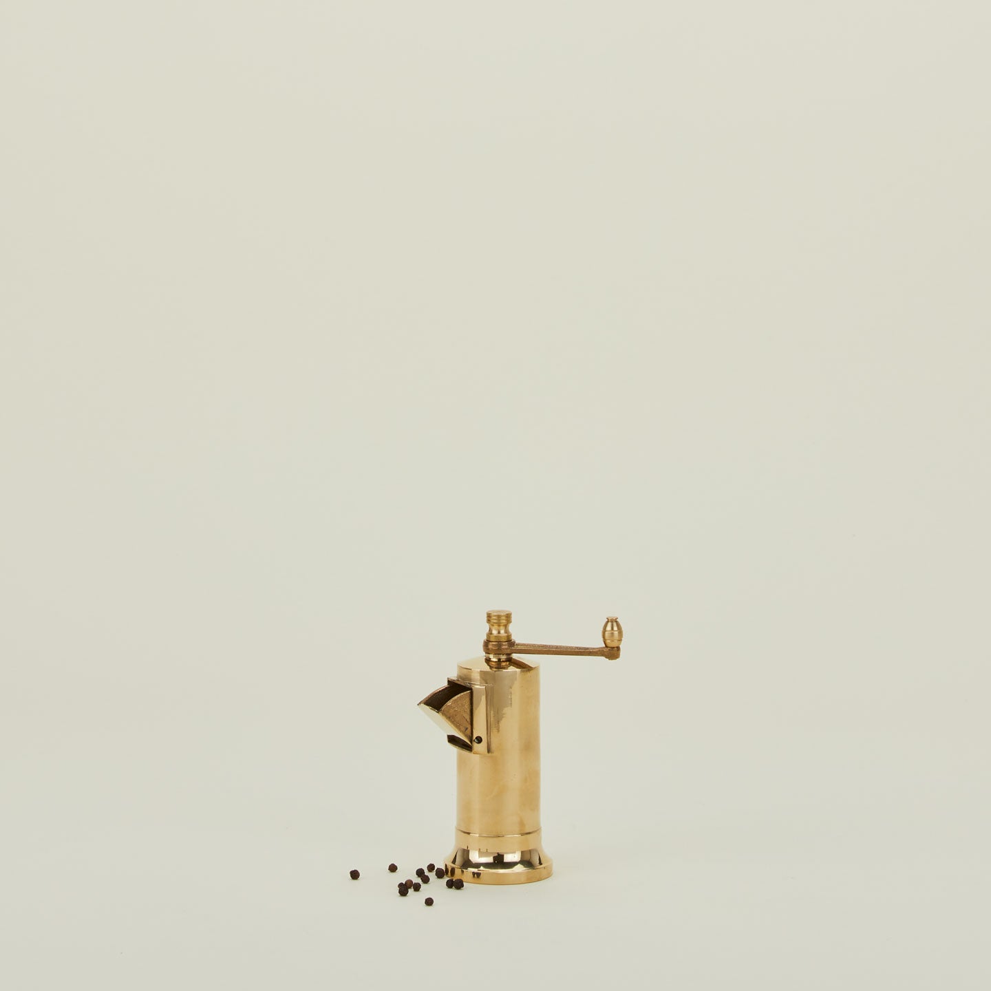 A brass spice grinder with handle, with peppercorns.