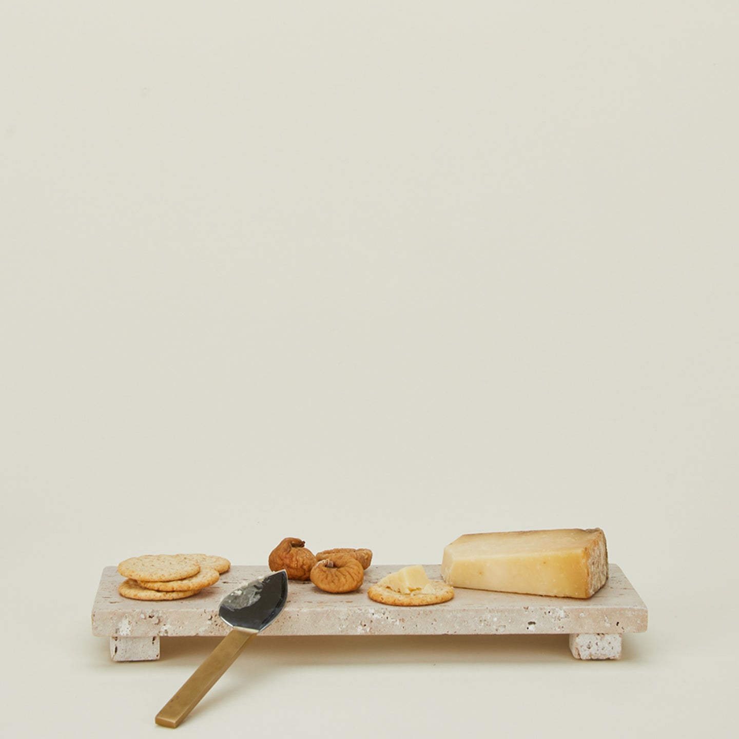 Travertine footed serving board with cheese, cheese knife, crackers, and dried fruit