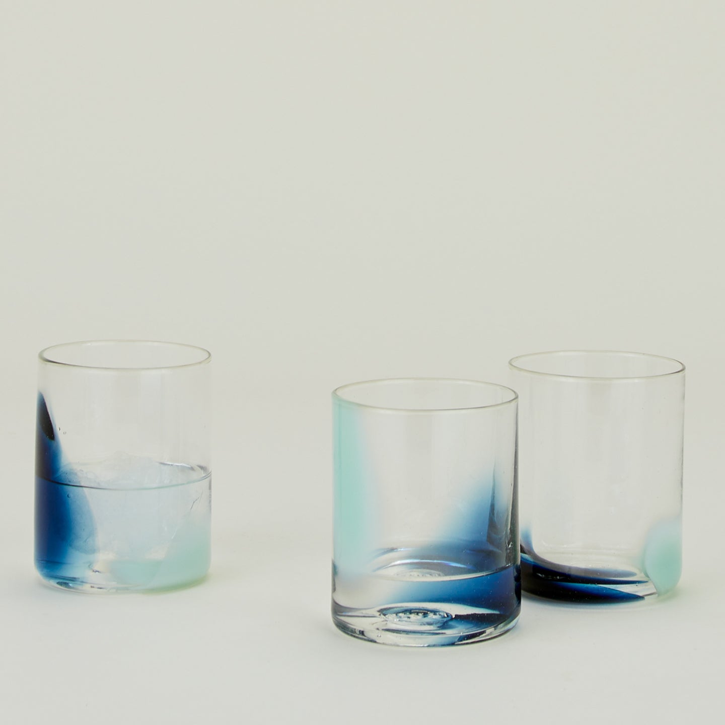 Three Blown Glass Tumblers in Sky and Peacock, filled with ice water.