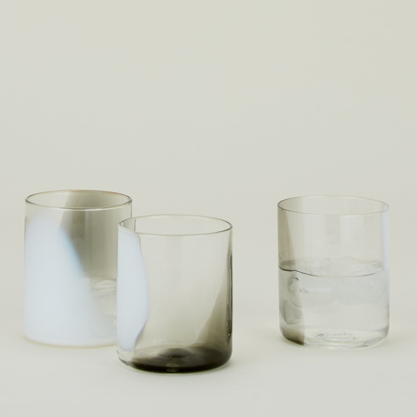 Three Blown Glass Tumblers in White and Grey, filled with ice water.