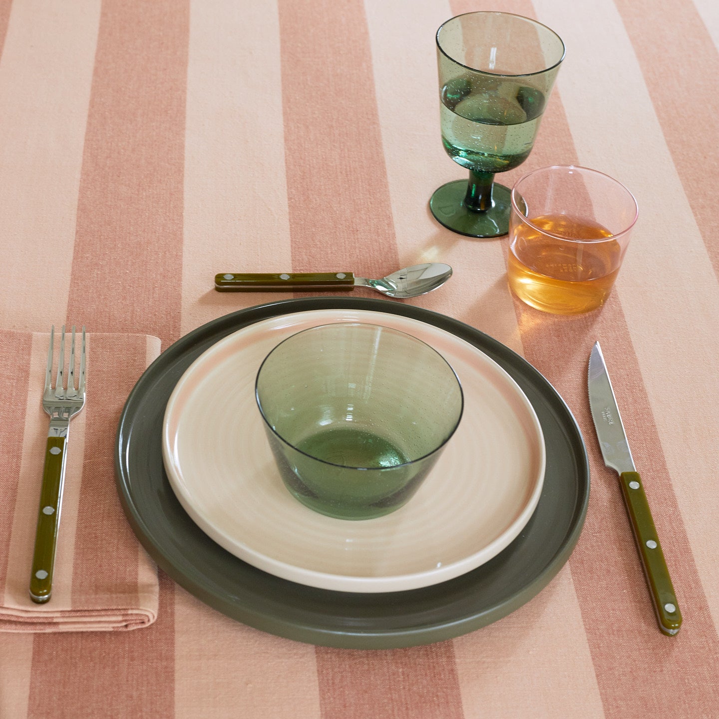 Placesetting with Glass Bowl in Jade on pink striped tablecloth.
