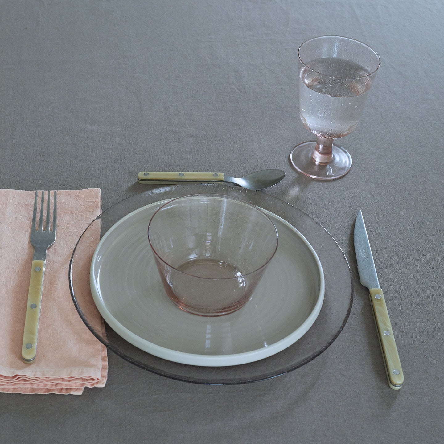 Placesetting with Glass Dinner Plate in Blush on grey tablecloth.