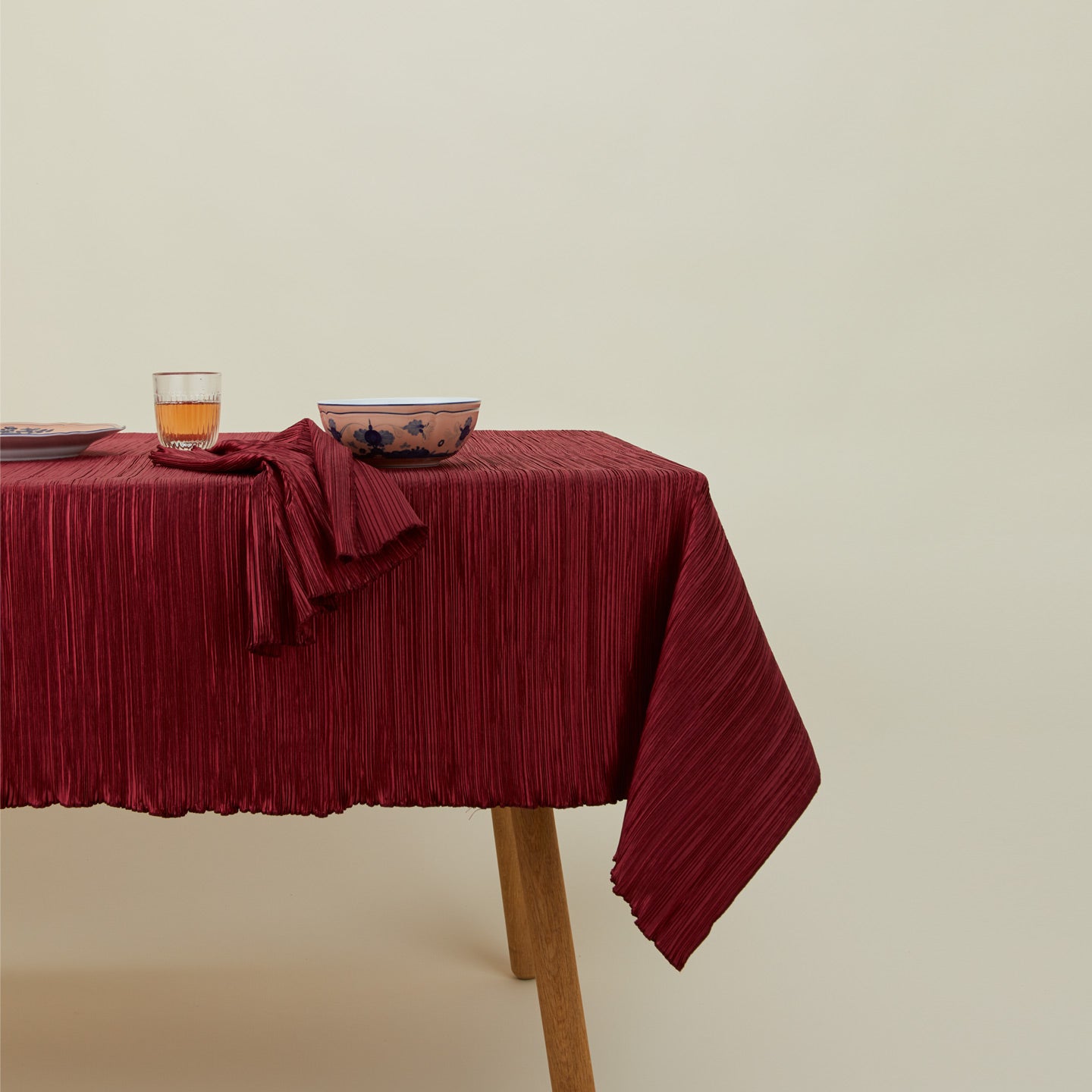 Cahaya pleated tablecloth in red on table with napkin, bowl, glassware, and plate