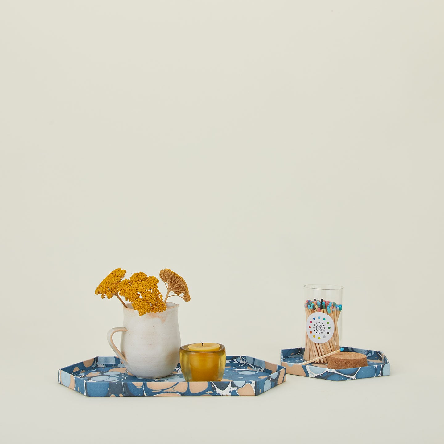 Set of two hexagon marbled trays in cool tones with a vase, votive, and matches.