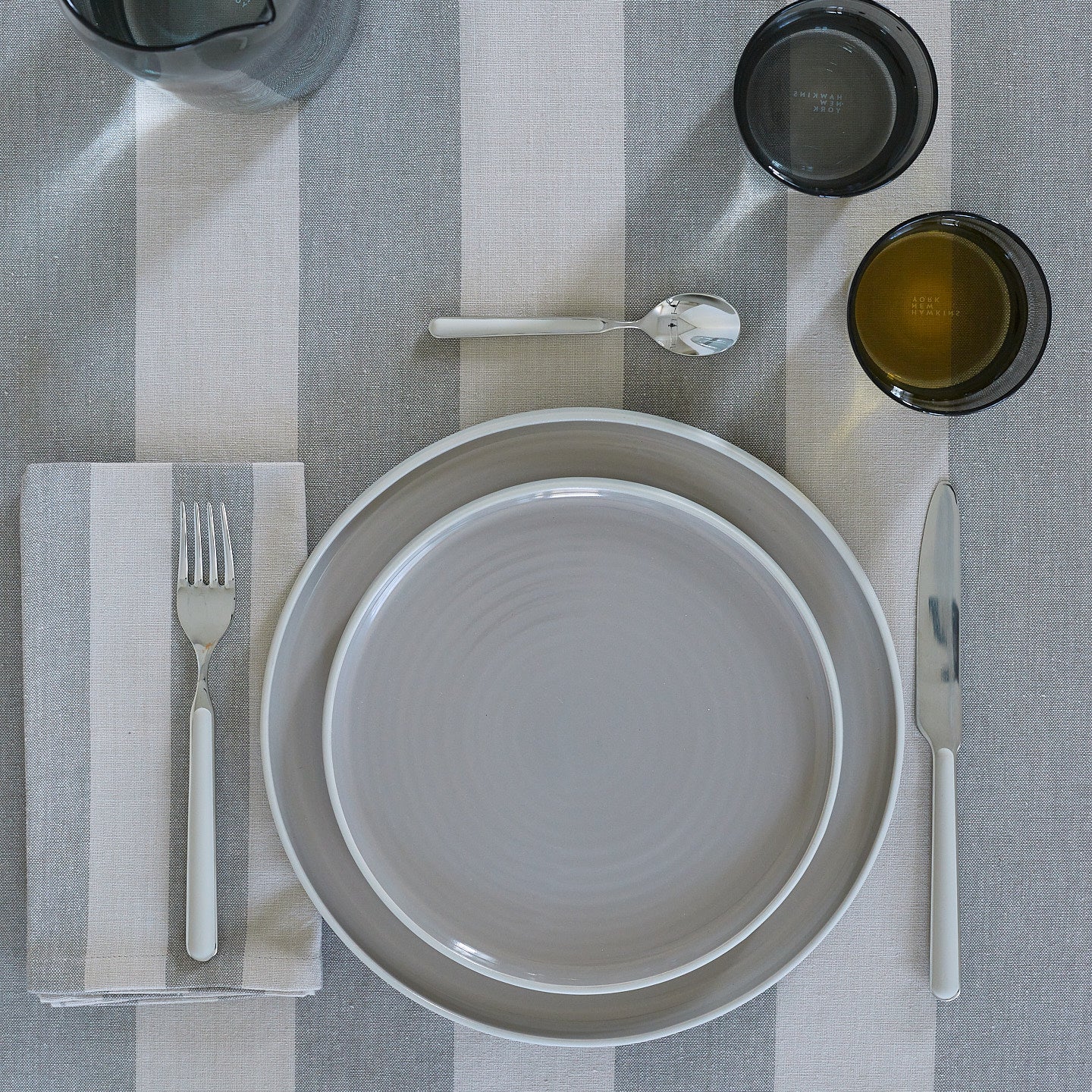 Placesetting with Essential Dinner Plate in Light Grey on grey striped tablecloth.