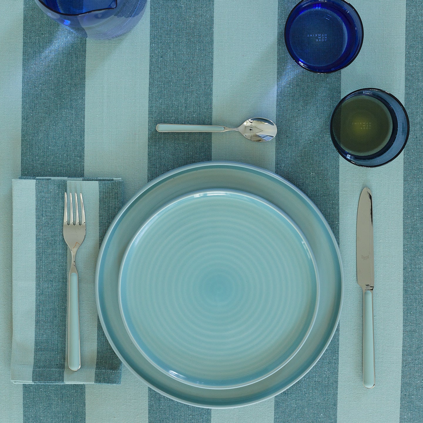 Placesetting with Essential Dinner Plate in Sky on blue striped tablecloth.