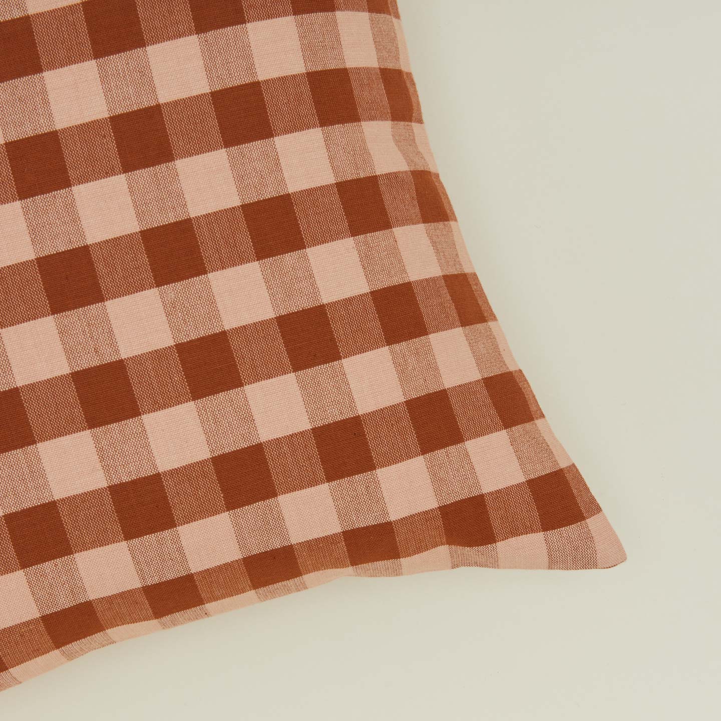 Close up view of gingham square pillow in blush/terracotta