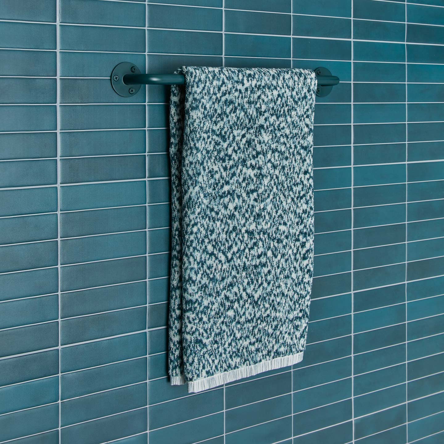Essential towel bar in Dark Peacock with Space Dye terry hand towel in Peacock on tiled wall.