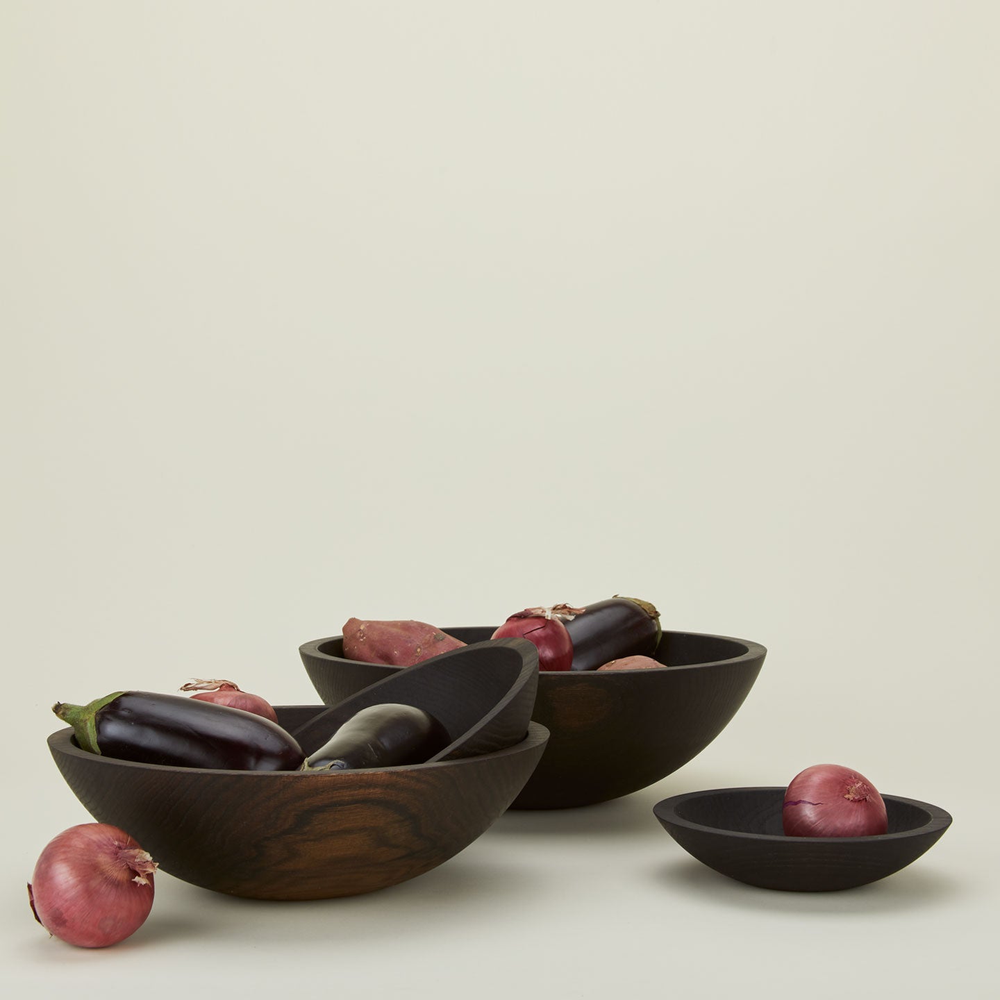 A group of ebonized oak wood bowls in four sizes, with produce.