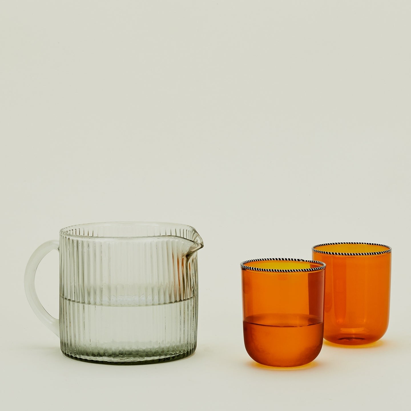 Glass Ribbed Pitcher, filled with water, along with two orange glass drinking glasses.