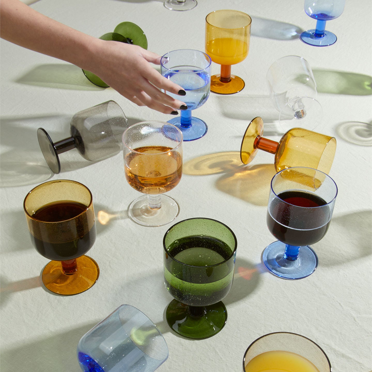 Simple seeded glassware in various colors with hand reaching in from the left.