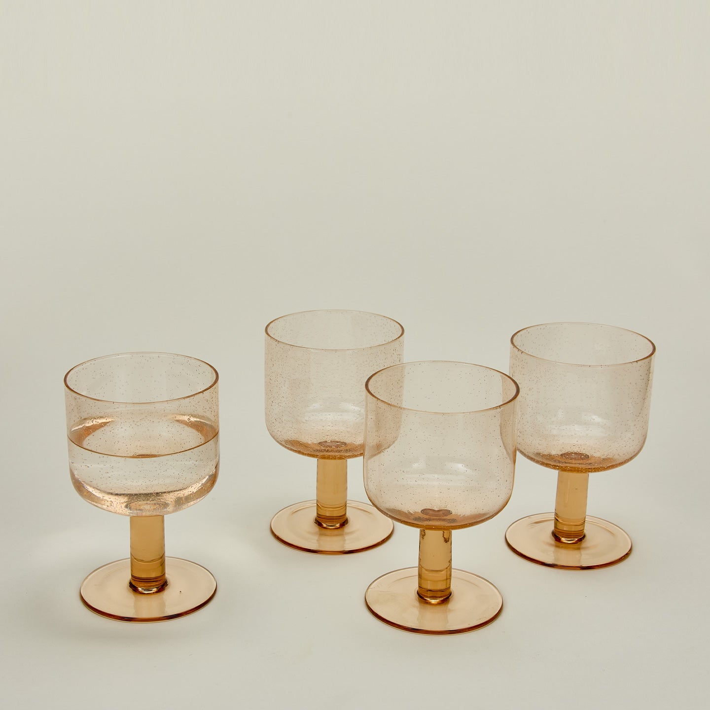 Three quarter view of Simple seeded glassware in Peach with water.