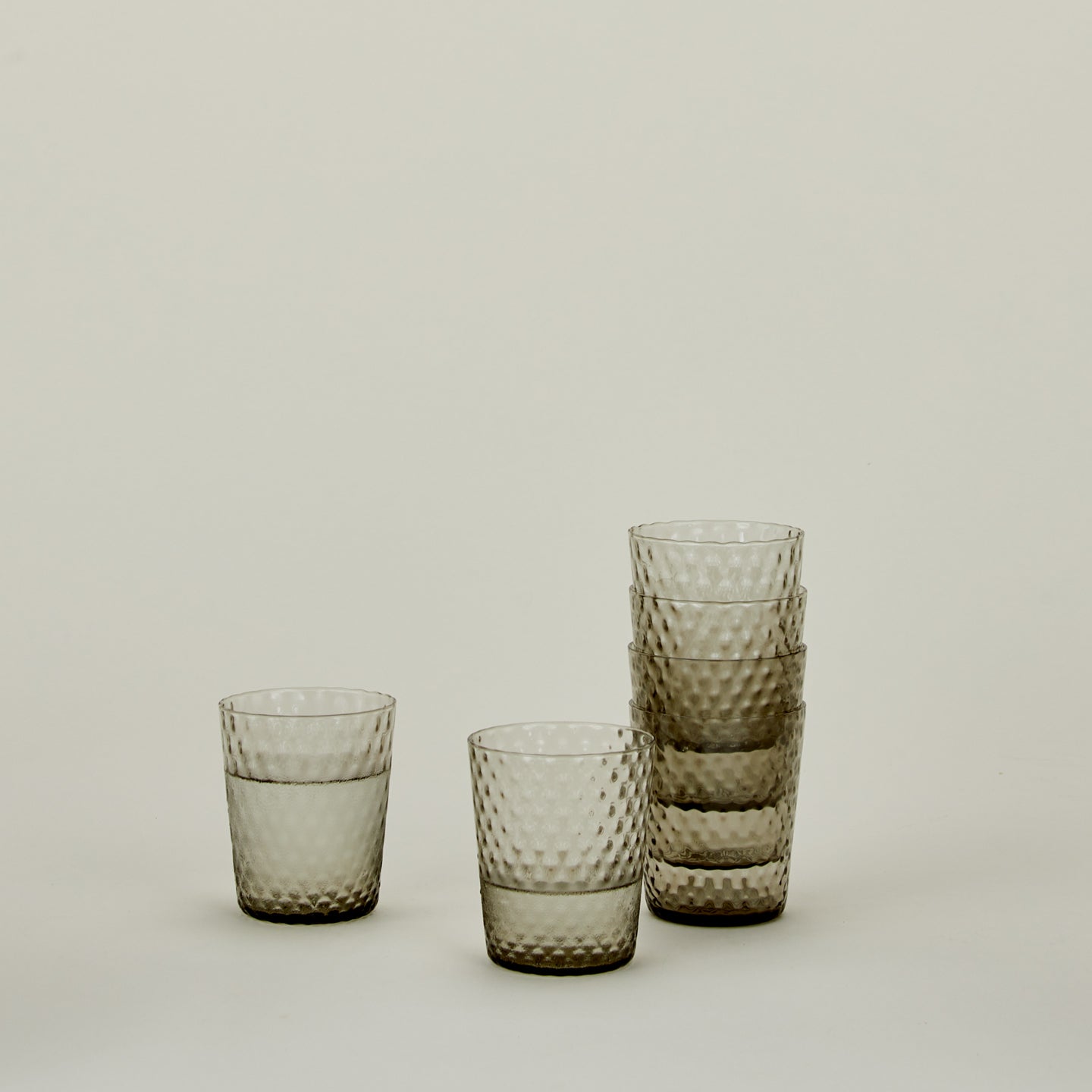 Set of 6 Veneziano Tumblers in Grey, stacked, with water.