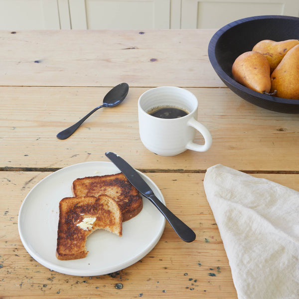 Toast on a table with coffee, a black wooden bowl, and a linen napkin.