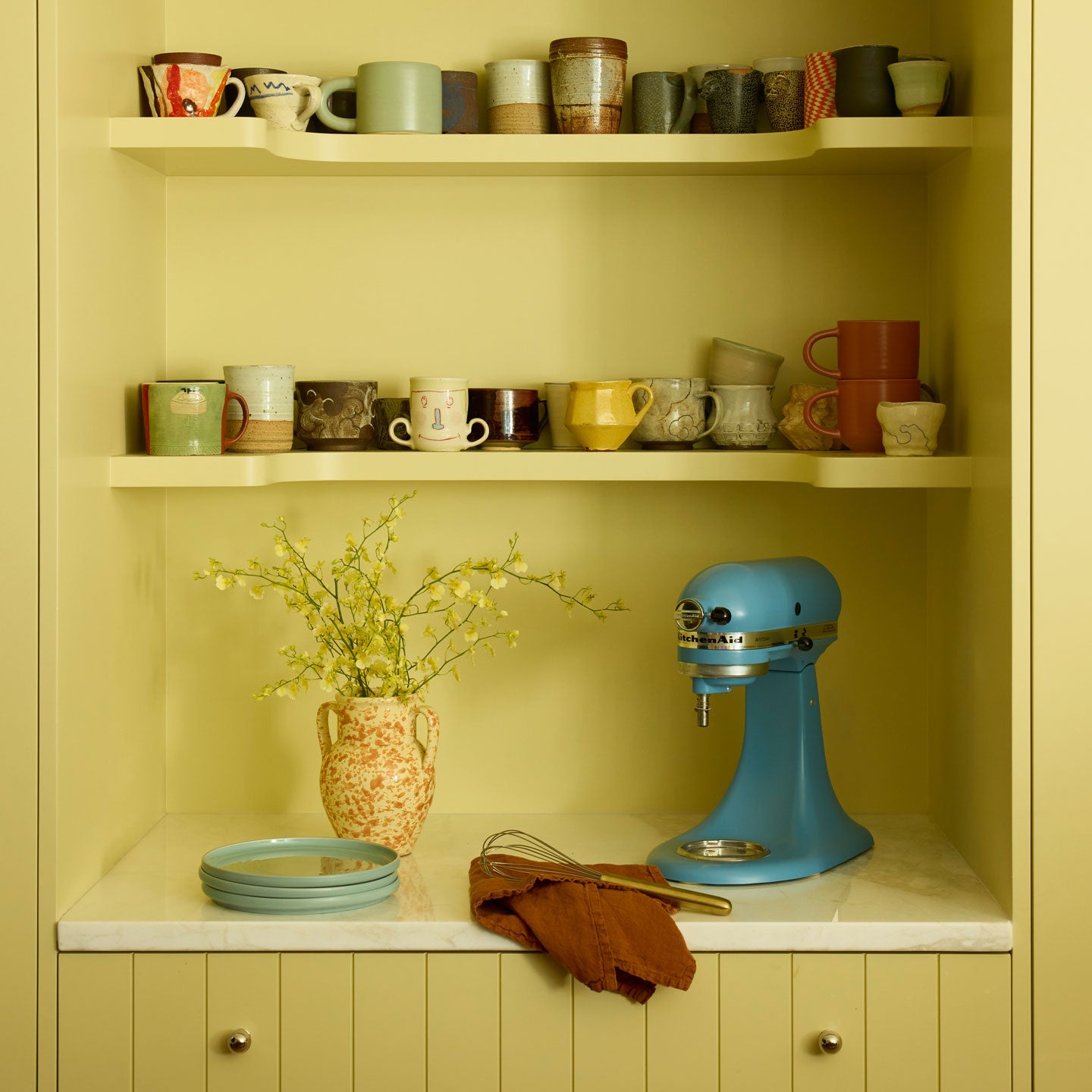 Kitchen shelving with mugs, kitchen aid, and vase.
