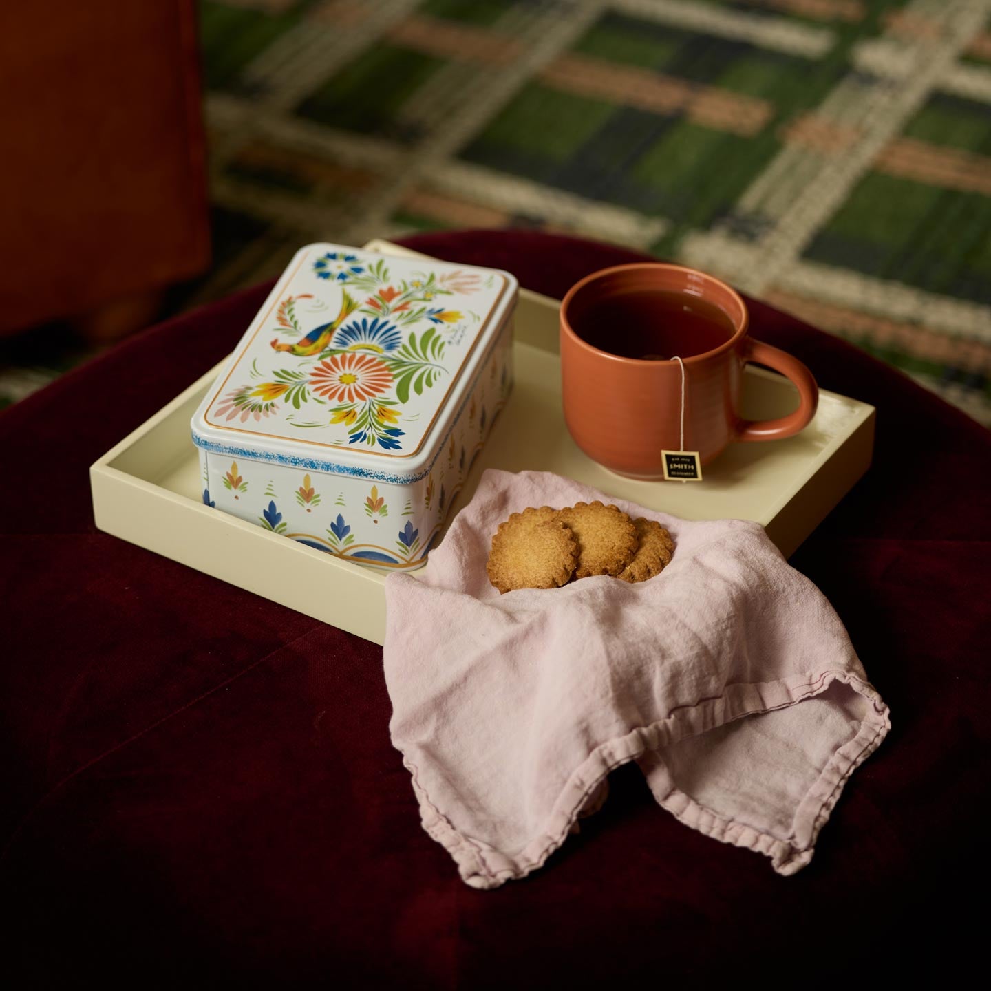 Tray with mug, painted tin, cookies and napkin on coffee table.