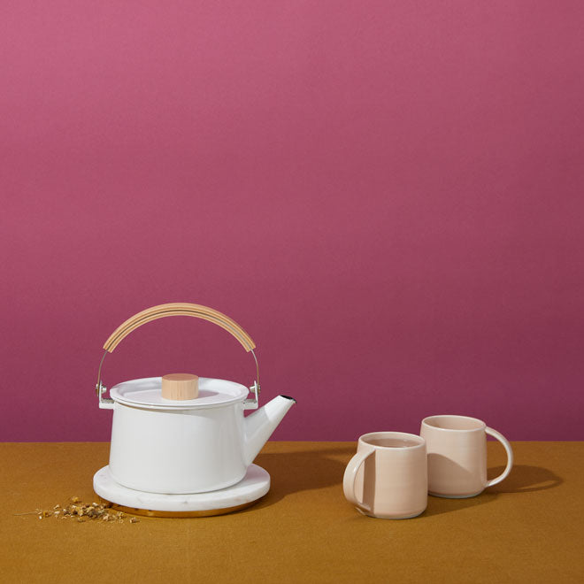 white tea kettle and two light pink mugs on dark pink background