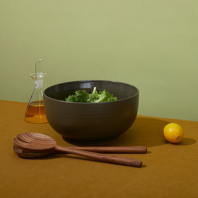large salad bowl, walnut wood salad servers and oil bottle styled with lemon on green background