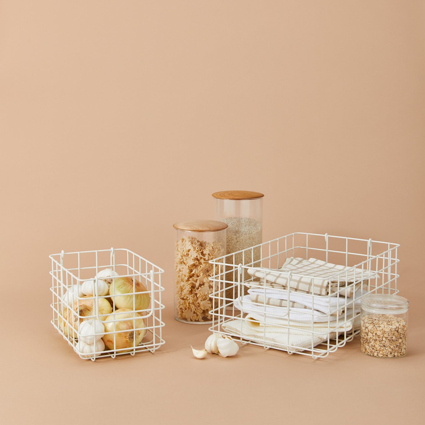 Mustard grid baskets with onions, garlic, kitchen towels and wood topped canisters filled with ingredients on a beige backgrouns.