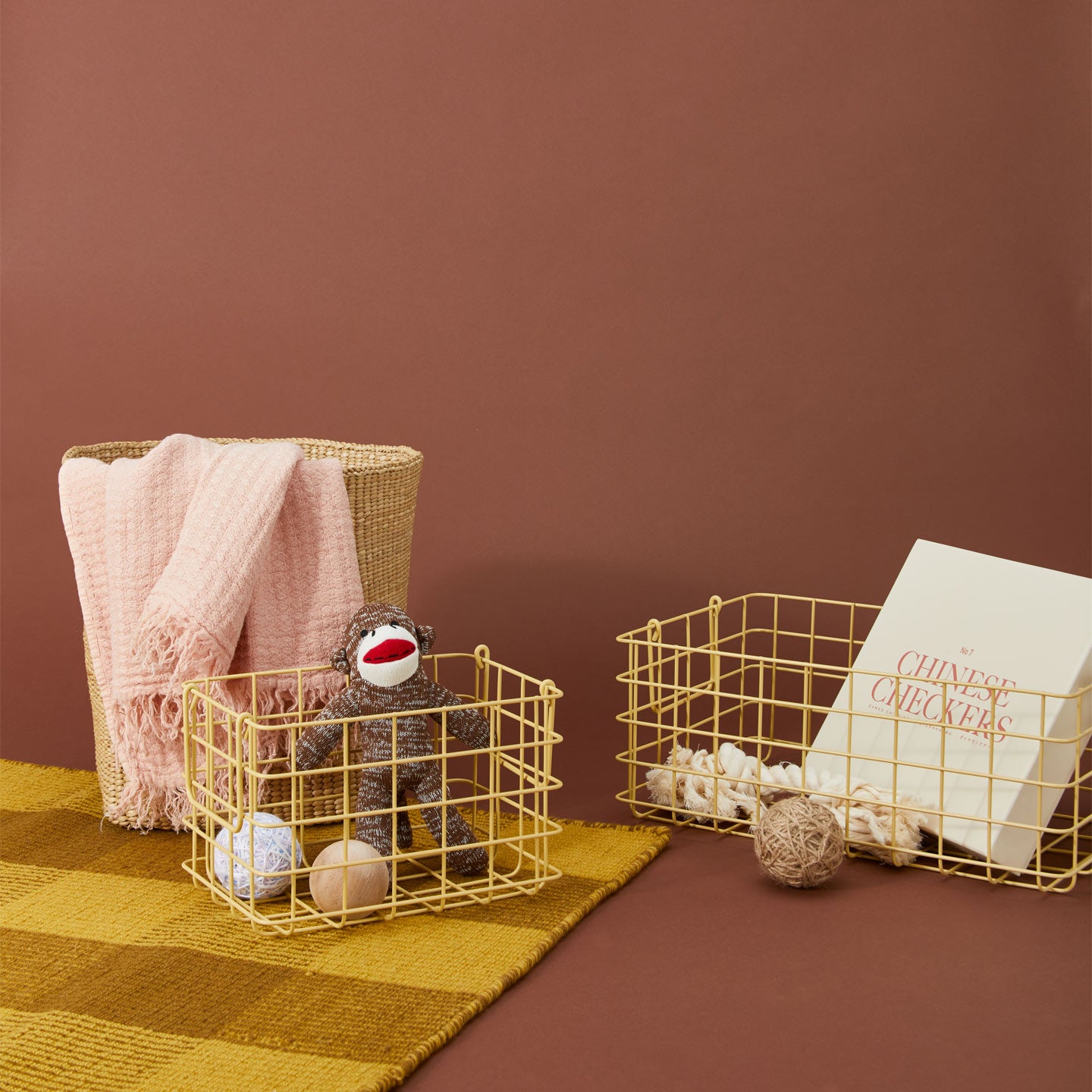 Gri baskets in butter with with games, yarn and a sock monkey. A basket with a blanket, all on a gingham carpet.