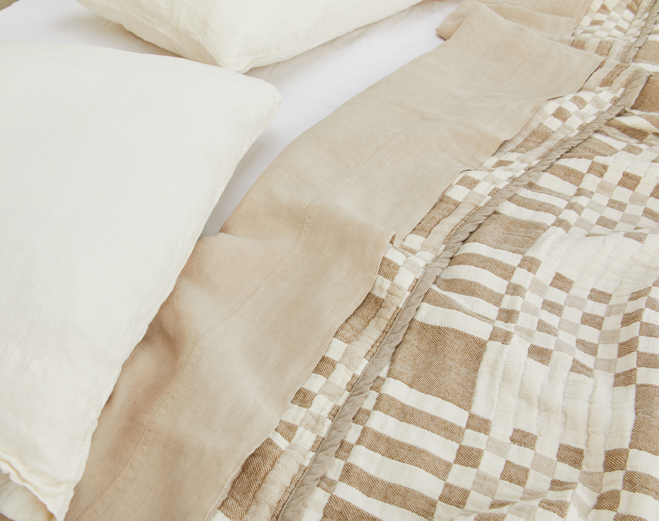 Close-up of beige and white checkered quilt with pillows in the background