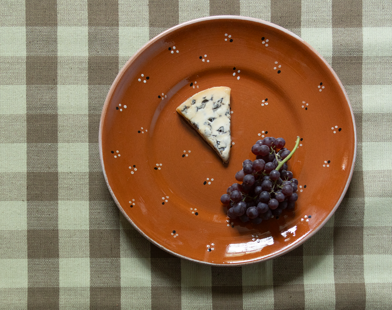 Orange plate with a wedge of blue cheese and grapes on a checkered tablecloth