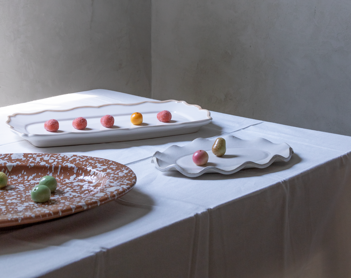 Assorted colorful marzipan candies on serving platters arranged on a white tablecloth covered table.