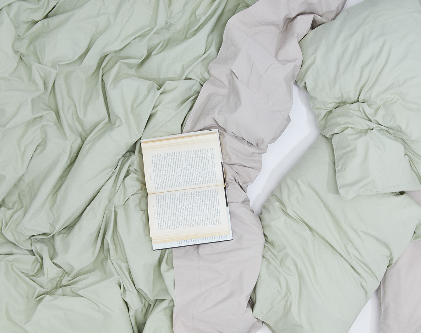 Green, grey and white bedding layers. Styled with an open book.