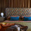Bed with patterned headboard, terracotta, bronze, and peacock bedding with multicolor throw.