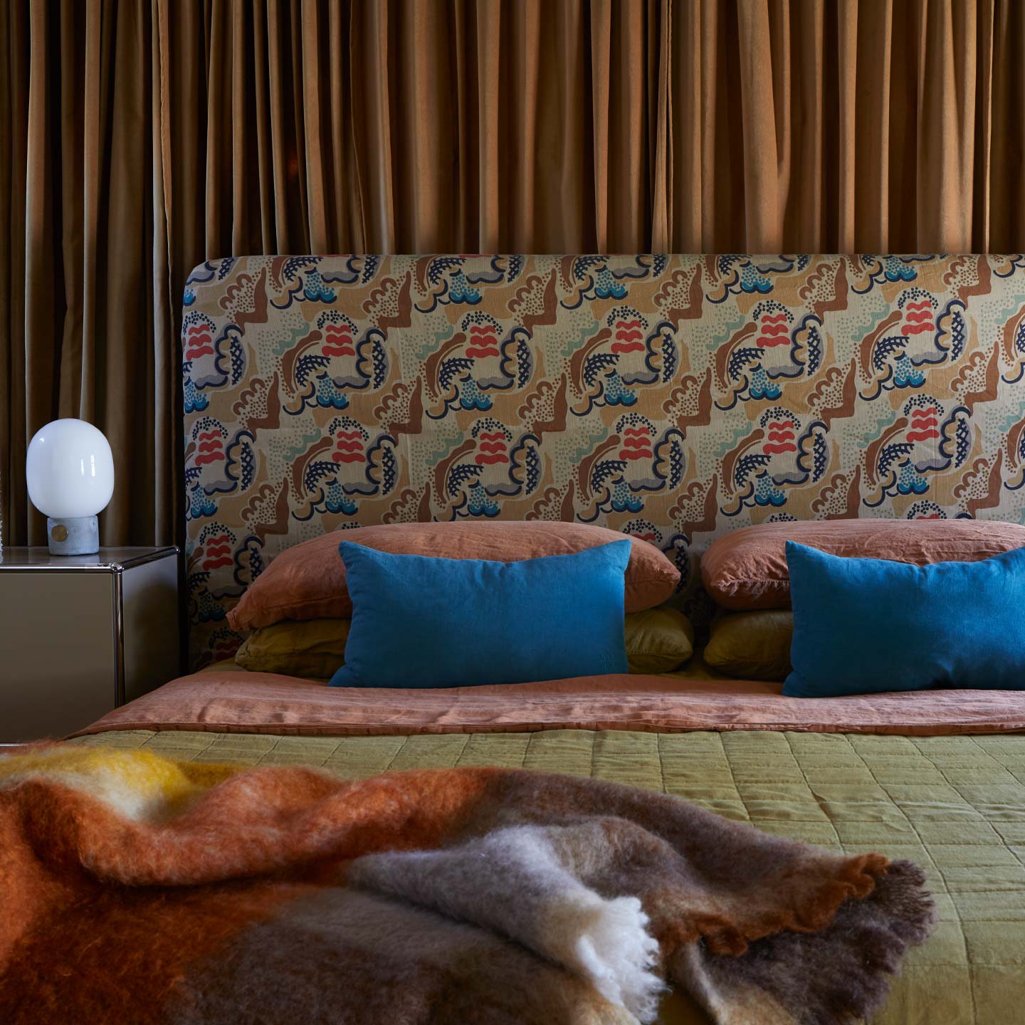 Bed with patterned headboard and colorful bedding in a bedroom setting.