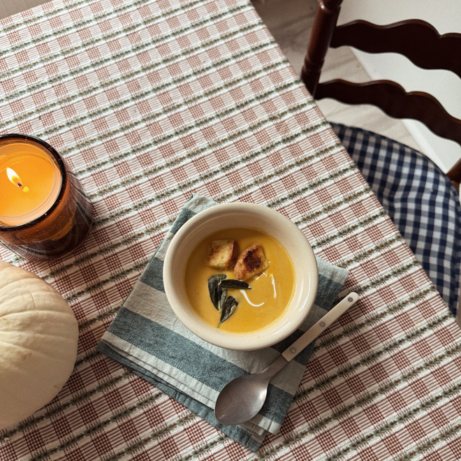 Bowl of soup with croutons and a candle on a checkered tablecloth