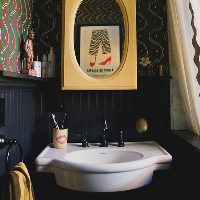 Bathroom sink with mirror and decorative elements on a dark wall.