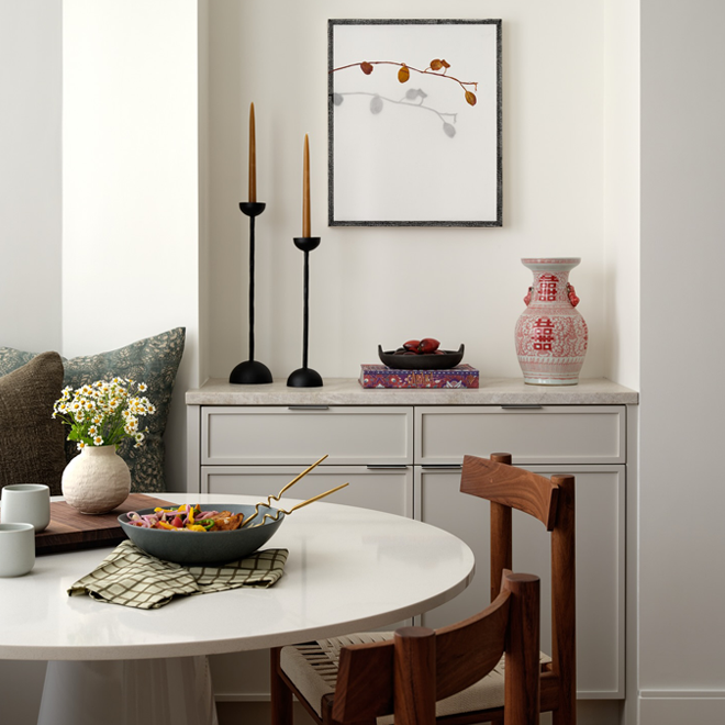 Dining room with a round table, chairs, and decorative items on a shelf.