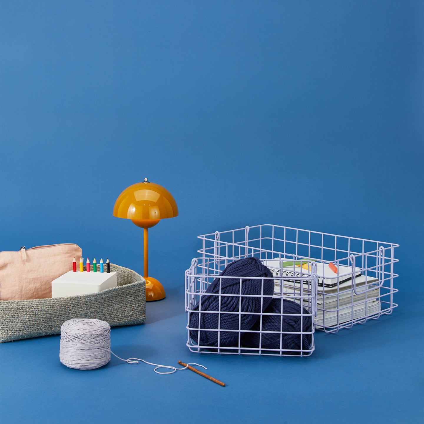 A yellow lamp and knitting and crafting supplies in wire and woven storage baskets against a blue background.