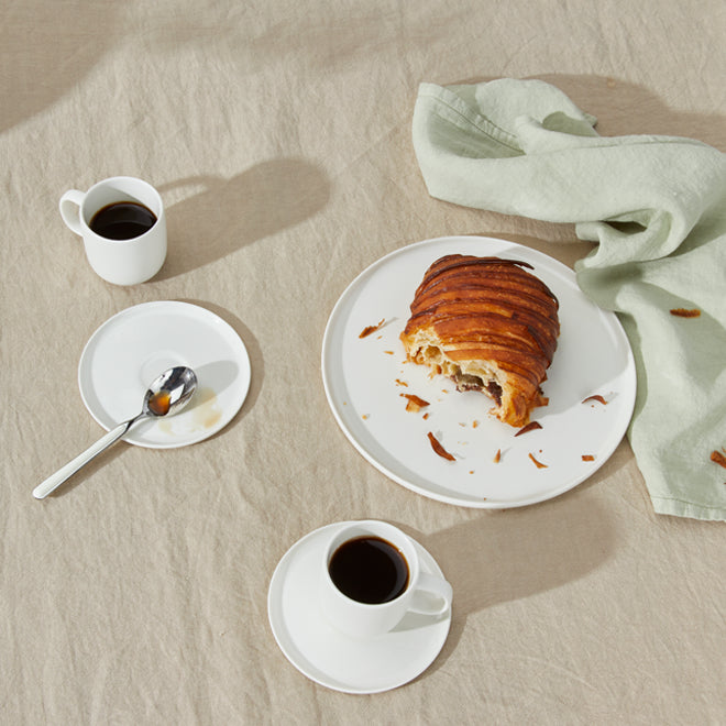 Breakfast scene with a croissant, coffee, and a napkin on a beige surface