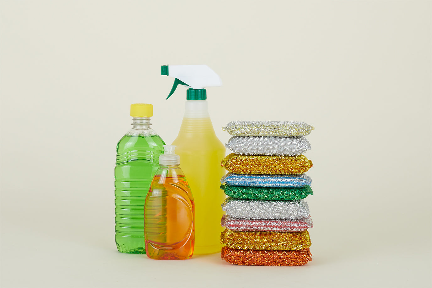 A stack of sparkly Lurex Sponges next to several bottles of brightly colored household cleaning products.