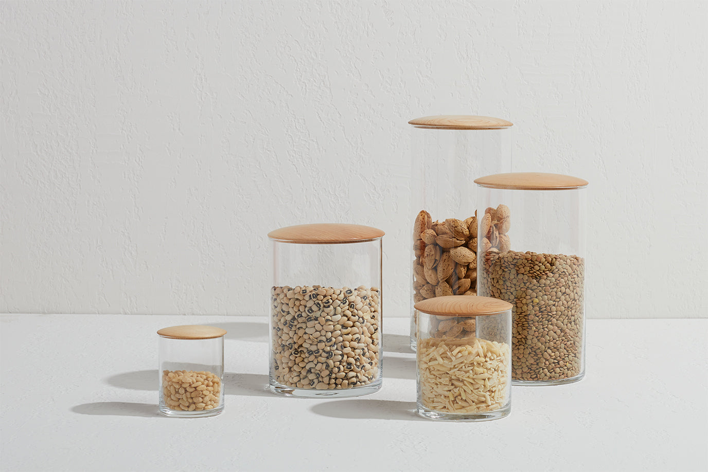 Glass storage containers with maple wood tops filled with dry goods including nuts, grains, beans and lentils.