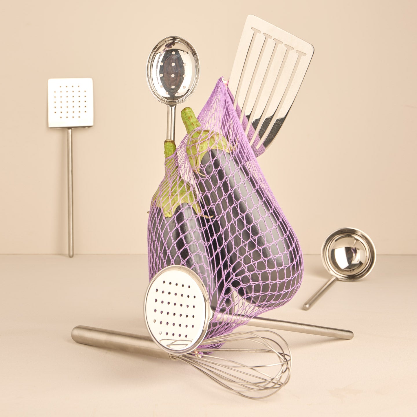 Simple metal kitchen tools in silver with net and eggplant on warm background.