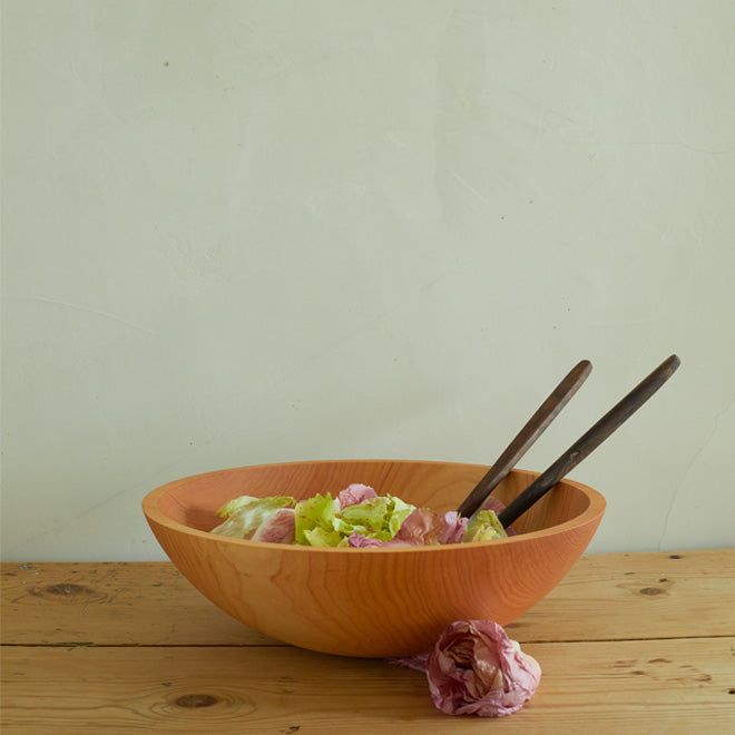 Wooden salad bowl and serving utensils with lettuces on wooden countertop.